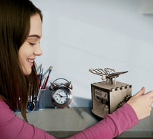 将图片加载到图库查看器，Model shown smiling while cranking wheel of automaton. The automaton is placed on desk.

